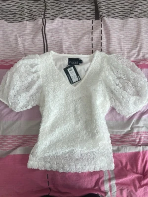Vit romantisk topp från Pieces med vackert ros-texturerat tyg och puffärmar - Superfeminin och elegant modell som passar perfekt till sommar, fest, student eller middagar. Tyget har fina rosdetaljer som gör toppen extra unik ✨