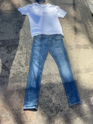 Blå slim fit jeans - Snygga blå slim fit jeans med klassisk femficksdesign och dragkedjegylf. Jeansen har en lätt tvättad look och smal passform som sitter tajt längs benen. Perfekta för en avslappnad och trendig stil.