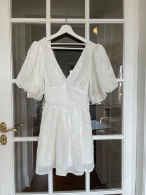 Gina Tricot embroided mini dress - Vit klänning med broderade detaljer från Gina Tricot. Knytning i ryggen, v-ringning, normal passform. Helt ny med etiketten kvar. Perfekt studentklänning! 