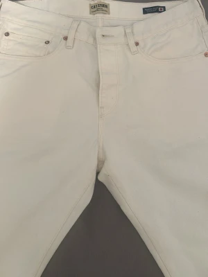 Vita jeans från C.O.F Studio - Snygga vita jeans från C.O.F Studio med klassisk femficksdesign och raka ben. Jeansen är tillverkade i kraftig denim och har en stilren look med läderpatch bak i midjan. Perfekta för dig som gillar minimalistisk och clean stil.