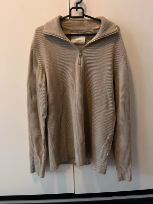Beige stickad halvzip-tröja - Snygg beige stickad tröja med halvzip och krage. Tröjan har ribbad struktur och långa ärmar, perfekt för lager-på-lager. Enkel och stilren design som passar till det mesta.