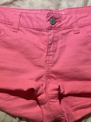 Rosa jeansshorts med fickor - Snygga rosa jeansshorts med klassisk femficksdesign och bälteshällor. Shortsen har knapp och dragkedja framtill samt uppvikta benslut. Perfekta för varma dagar och en färgstark look. Pris kan diskuteras🩷