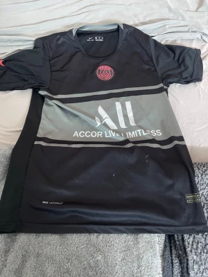 Svart PSG Messi matchtröja Nike - Snygg svart PSG matchtröja från Nike med Messi 30-tryck på ryggen. Tröjan har gråa detaljer, klubbmärke på bröstet och sponsorlogga framtill. Tillverkad i lätt och ventilerande material, perfekt för fotbollsträning eller att bära som supporter.