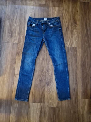 Jeans från lager 157 - Snygga blå slim fit jeans från Lager 157 med klassisk femficksdesign och normalhög midja. Jeansen har en mörk tvätt och raka ben, perfekta till en avslappnad stil. Tillverkade i bomull med lite stretch för extra komfort.