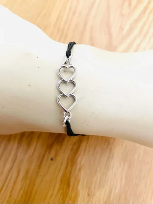 By prisförslag- Armband med tre hjärtan i silverfärg justerbart  - Snyggt armband med tre sammankopplade hjärtan i silverfärgad metall och svart justerbart band. Hjärtana har en öppen design som ger en stilren och modern look. Perfekt accessoar för dig som gillar minimalistiska smycken och vill addera lite kärlek till din stil.