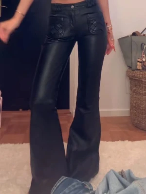 Svarta utsvängda läderbyxor Zadig & Voltaire - Säljer ett par svarta jeans med skinnlook och utsvängda ben. Jeansen har hög midja, dekorativa fickor fram och en glansig finish som ger en cool vibe. Perfekta för dig som vill sticka ut och gillar trendiga detaljer.