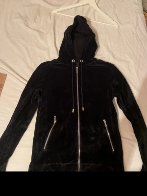 Limitato zip-hoodie - svart limitato hoodie i mjukt velourmaterial med huva och snören. Två snedställda dragkedjefickor framtill och ett stort fototryck på ryggen. Perfekt för dig som gillar unika detaljer.