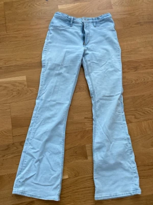 Ljusblå bootcut jeans H&M - Säljer ett par ljusblå jeans med bootcut passform. Jeansen är tillverkade i ett mjukt jeansmaterial.  Vid midjan går det att göra midjan tajtare med två knappar och ett band. De är klassiska jeans som man kan göra mycket med , sy om/ göra hål/ osv.