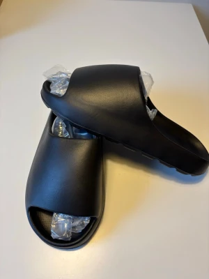 Yeezy slides svarta likande  - Svarta Yeezy slides liknande. Dom är helt nya och oanvända. Dom passar storlek 43.