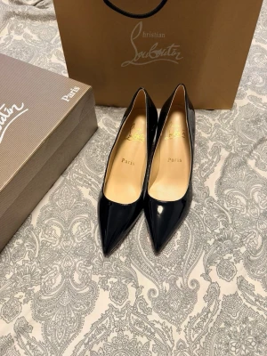 Svarta lackpumps från Christian Louboutin - Stilrena svarta pumps i lack från Christian Louboutin med spetsig tå och klassisk design. Skorna har en elegant siluett och ikonisk röd sula. Perfekta för dig som vill ha en lyxig och tidlös sko i garderoben.
