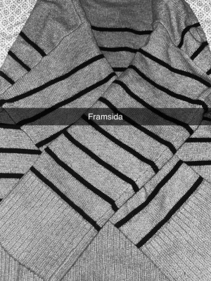 Grå stickad tröja med svarta ränder - Snygg stickad tröja i grått med svarta horisontella ränder. Tröjan har långa ärmar och ribbstickade muddar vid ärmslut och nederkant. Perfekt för en chill och stilren look. Materialet känns mjukt och bekvämt.