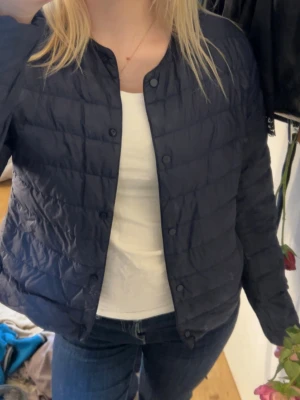 Uniqlo jacka - Stilren mörkblå vindjacka med quiltat mönster och tryckknappar framtill. Jackan har rundad krage och raka ärmar. Perfekt för dig som vill ha en lätt och enkel jacka till vardagslooken.