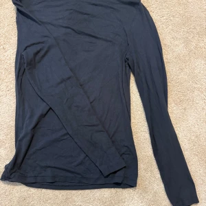 Svart långärmad topp från 157 - En enkel svart långärmad topp från 157. Modellen är rak med rund halsringning och tillverkad i ett mjukt, tunt material som känns skönt mot huden. Perfekt att styla lager på lager eller bära som den är.