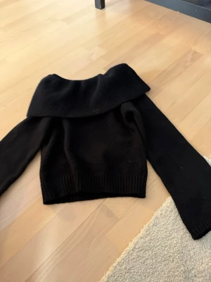 Svart off shoulder stickad tröja SHEIN - Trendig svart stickad tröja från SHEIN med bred off shoulder-krage och långa ärmar. Ribbstickade muddar vid ärmslut och nederkant. Perfekt för dig som vill ha en snygg och bekväm look till hösten eller vintern.