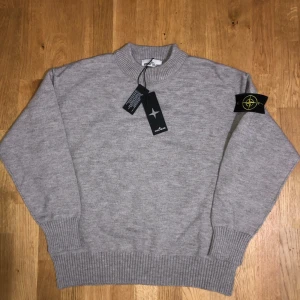 Stone Island Tröja - Stickad tröja från Stone Island i klassisk ljusgrå färg. Rund hals, ribbade muddar och nederkant samt den ikoniska Stone Island-badgen på ärmen. Storlek M med normal passform. Helt ny, aldrig använd. Originaltags medföljer. Skickas snabbt och säkert vid affär.