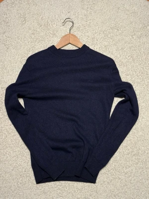 Mörkblå stickad tröja Lindbergh - Mörkblå stickad tröja från Lindbergh med rund halsringning och ribbade muddar vid ärmslut och nederkant. Klassisk och enkel design som passar perfekt till lager på lager. Materialet känns mjukt och bekvämt.