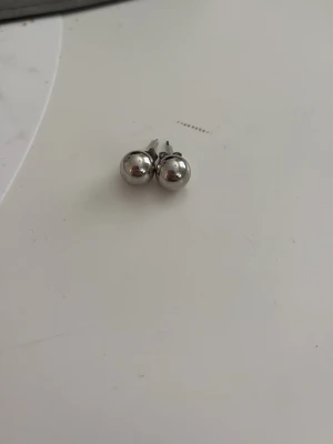 Pärlörhängen i silverfärgat material  - Säljer ett par pärlörhängen i silverfärgat material. De är i metall med sopolerad, blank yta och klassisk design som passar till det mesta. Perfekta för dig som gillar minimalistiska accessoarer. Från Kappahl aldrig använt, kanske kan färga av sig men jag vet inte. Jag har råkat tappa bort en plupp till örhänget men ersatt den med en ny så de är inte likadana, se bild 2