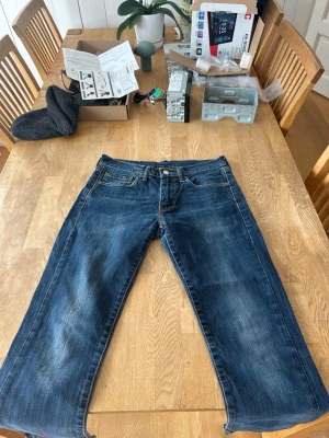 Levi's blå raka jeans - Klassiska blå jeans från Levi's med rak passform och fem fickor. Jeansen har slitningar och kontrastsömmar samt en ikonisk läderpatch bak i midjan. Tillverkade i slitstark denim med en snygg tvättad look.