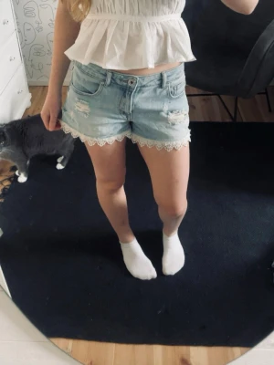 Ljusblå jeansshorts med spetskant - Säljer ett par ljusblå jeansshorts med snygga slitningar och dekorativ vit spetskant🤍
