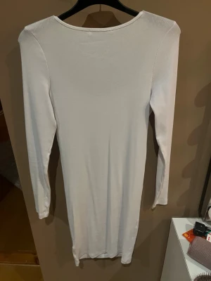 Vit ribbad långärmad klänning - Säljer en enkel och stilren vit klänning från H&M. Klänningen är ribbad, har lång ärm och en rundad urringning. Modellen är kroppsnära och går till strax ovanför knäna. Perfekt för dig som gillar minimalistisk stil.