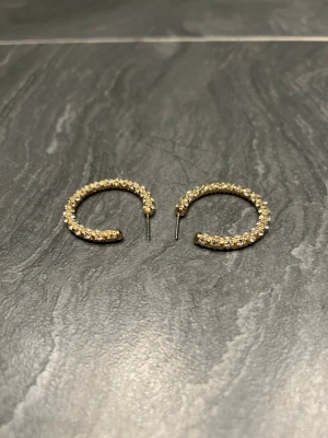 Eleganta örhängen! - Snygga örhängen i form av halvöppna hoops i guldfärg, täckta med små gnistrande stenar som ger en lyxig känsla. Perfekta för att lyfta din stil med lite extra bling. Materialet är troligen metall med infattade stenar. Märke saknas.