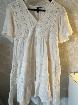 Studentklänning med broderade blommor - Söt vit kortklänning med v-ringning och korta ärmar. Klänningen har broderade blommor och volangdetaljer. Luftig och bekväm, perfekt för varma dagar! Kan passa som studentklänning❗️