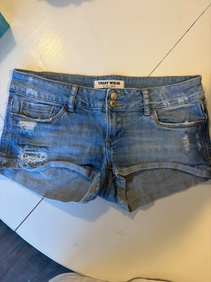 Lågmidjade jeansshorts från Tally Weijl - Säljer ett par blå denimshorts från Tally Weijl med slitna detaljer och rå kant. Klassisk femficksdesign, låg midja och knappstängning framtill. Pris går att diskutera💕