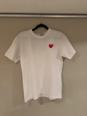 Vit Comme des Garçons Play t-shirt - Vit t-shirt från Comme des Garçons Play med det ikoniska röda hjärtat med ögon broderat på bröstet. Klassisk passform och rund halsringning. Perfekt basic-plagg med en twist som funkar till allt.