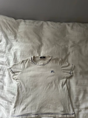 Vit t-shirt från J.Lindeberg - Vit t-shirt från J.Lindeberg med blå kontrastsömmar och liten broderad logga på bröstet. T-shirten är i storlek M men skulle säga att den passar xs- ev s väldigt liten i storleken💕 passar perfekt för en stilren outfit i sommar☀️sömmarna har blivit lite sämre ( se sista bild)