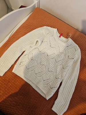 Vit stickad tröja från H&M - Säljer en vit stickad tröja från H&M med snyggt hålmönster och rund hals. Tröjan har långa ärmar och ribbade muddar vid ärmslut och nederkant. Perfekt för dig som gillar en enkel men trendig look.