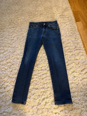 Mörkblå slim jeans från J.Lindeberg - Snygga mörkblå slim fit jeans från J.Lindeberg med klassisk femficksdesign och lätt slitning på låren. Jeansen har normal midja och raka ben, perfekta för en stilren vardagslook. Tillverkade i mjuk denim med stretch för extra komfort.