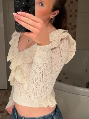 Vit stickad blus med spetsvolanger - Supersöt vit stickad blus med djup ringning och spetsvolanger.