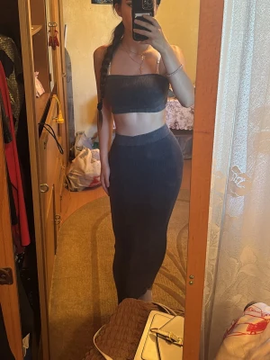 Mörkgrå ribbat set med tubtop - Säljer ett mörkgrått ribbat set bestående av en tubtop och en lång, figurnära kjol. Setet är i mjukt och stretchigt material som sitter snyggt på kroppen. Använd bara en gång, köptes från New Yorker.