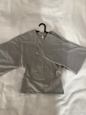 Grå långärmad topp från H&M - En stilren grå långärmad topp med tajt passform och vida ärmar. 