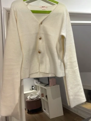 Vit kofta med knappar - Stilren vit kofta med v-ringning och tre bruna knappar framtill. Koftan har långa ärmar och rak passform, perfekt för lager på lager. Materialet ser mjukt och bekvämt ut, vilket gör den enkel att matcha till olika outfits.