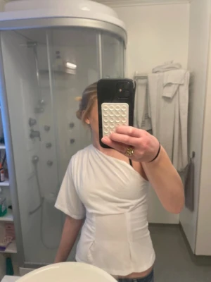 Vit oneshoulder topp med kort ärm - Säljer en vit oneshoulder topp i mjukt material. Toppen har en unik design med en ärm och ena axeln bar. Perfekt att styla med jeans eller kjol för en snygg outfit. Använt ett få antal gånger!!🥰❤️