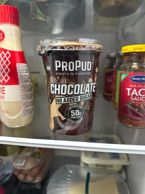 ProPud choklad proteinpudding - ProPud proteinpudding med chokladsmak, laktosfri och utan tillsatt socker. Innehåller 20g protein per bägare och har en krämig konsistens. Förpackningen är brun och beige med tydlig text och plastlock.