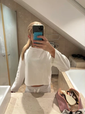 Vit croppad sweatshirt - Mysig vit croppad sweatshirt med långa ärmar och ribbad rund hals. Tröjan har en avslappnad passform och är gjord i mjukt material, perfekt för chill dagar. Enkel och stilren design som passar till det mesta.
