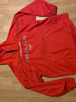 Röd Original Chicago Bulls Vintage 00s pull-over/sportjacket - Sällsynt Original Adidas Chicago Bulls anorak/windbreaker från tidigt 2000-tal (ca 2007). Storlek: US L / EU XL (se etikett). Material: 100% polyester. Skick: bra vintage-skick, se bilder. Adidas style 5972A 07, se bilder på etiketter