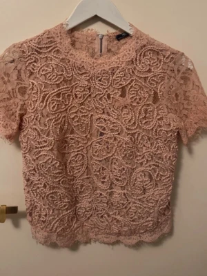 Beige spetsblus med kort ärm - Säljer en puderrosa spetsblus från Gina Tricot med korta ärmar och rund hals. Blusen har ett vackert blommigt spetsmönster och dragkedja i ryggen. Perfekt för dig som vill ha en feminin look.