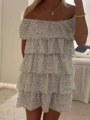 Vit offshoulder volangklänning zara - Supersöt vit offshoulder klänning med svarta prickar och flera lager volanger. Klänningen är kort och har en luftig passform, perfekt för varma dagar. 