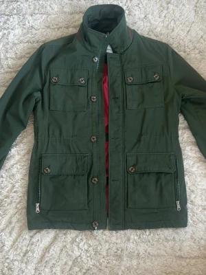 J Lindeberg Field Jacket - Grön field jacket från j Lindeberg. Väldigt bra skick förutom att två knappar saknas, en i ena framsida ficka och andra på baksidan. 