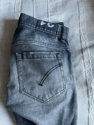 Grå slitna jeans från Cheap Monday - Säljer ett par grå jeans från dondup med slitningar och tvättad look. Klassisk femficksmodell med knappgylf och logga på linningen. Jeansen har en avslappnad passform och är tillverkade i bomull.