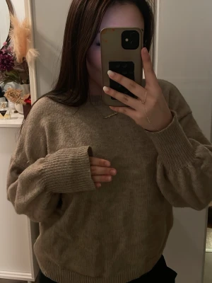 Beige oversized stickad tröja - Mysig beige stickad tröja med oversized passform och breda ribbade muddar vid ärmslut och nederkant. Tröjan har rund halsringning och är perfekt för lager-på-lager-stil. Materialet ser ut att vara mjukt och skönt.