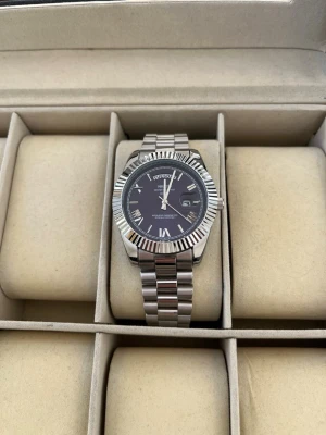 Ekstrand Daydate Blå/silver - Stilren klocka med silverfärgat metallarmband och blå urtavla. Klockan har romerska siffror, datumvisning och räfflad bezel. Perfekt accessoar för dig som gillar klassisk och tidlös design.