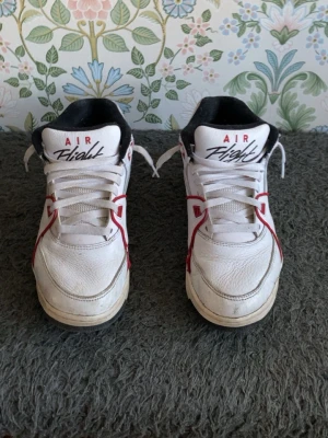 Nike Air Flight vita sneakers - Nike Air Flight sneakers i vitt läder med röda och svarta detaljer. Klassisk låg modell med svart vadderad insida och tydlig logga på plösen. Snygg retrostil och coola kontrastlinjer längs sidorna. Perfekta för dig som gillar old school vibes och streetwear.