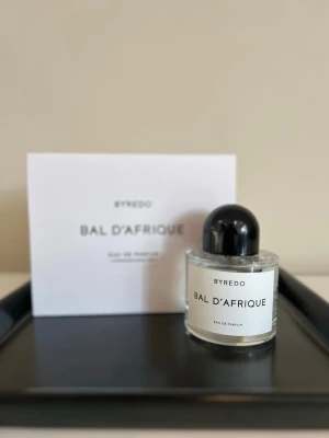 Byredo Bal d'Afrique Eau de Parfum - Byredo Bal d'Afrique Eau de Parfum i en stilren, rund glasflaska med svart rund kork och vit etikett. Doften är elegant och modern, och flaskan kommer med originalkartong i vitt. Perfekt för dig som gillar exklusiva och trendiga parfymer.