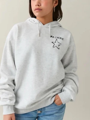 Grå hoodie med stjärna och text - Snygg ljusgrå hoodie med huva och dragsnören. På bröstet finns en svart stjärna och texten 'MA CHÉRIE'. Hoodien har en avslappnad passform och ribbade muddar vid ärmslut och nederkant. Perfekt för en chill och trendig look. Texten är lite bortskrapad från tvätten och mycket användning, tycker den ser snyggare ut så.🤗💕💐