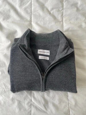 Grå merinoulltröja med dragkedja  - Mörkgrå tröja från These Glory Days i mjuk och lyxig merinoull. Tröjan har hel dragkedja framtill, hög krage och långa ärmar. Perfekt för lager-på-lager och stilren look. Enkel och tidlös design som passar till det mesta.