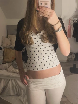 Vit prickig topp - Säljer en vit croppad linnetopp med svarta prickar och tunna axelband. Toppen har en lätt draperad urringning och är figurnära i modellen. Perfekt för dig som gillar en lekfull och trendig stil. Har behövt sytt om spännet pga tidigare ägare och det vart lite snurrigt, men går att sprätta upp och sy om om man vill. 